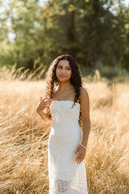 senior photos by a river in a field at sunset
