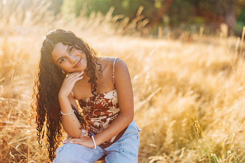 senior photos by a river in a field at sunset
