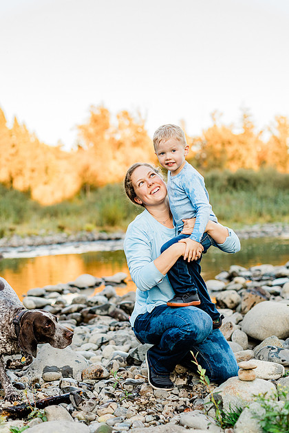 a boy, his mom and their dog playing by the river