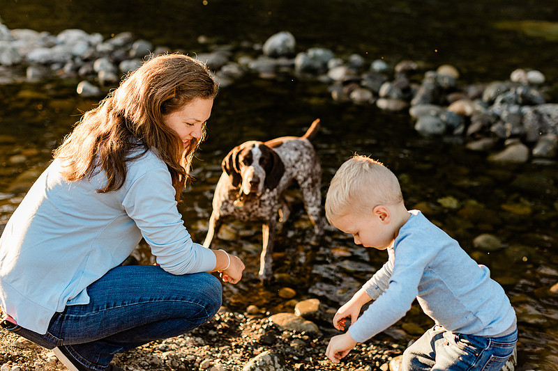 a boy, his mom and their dog playing by the river