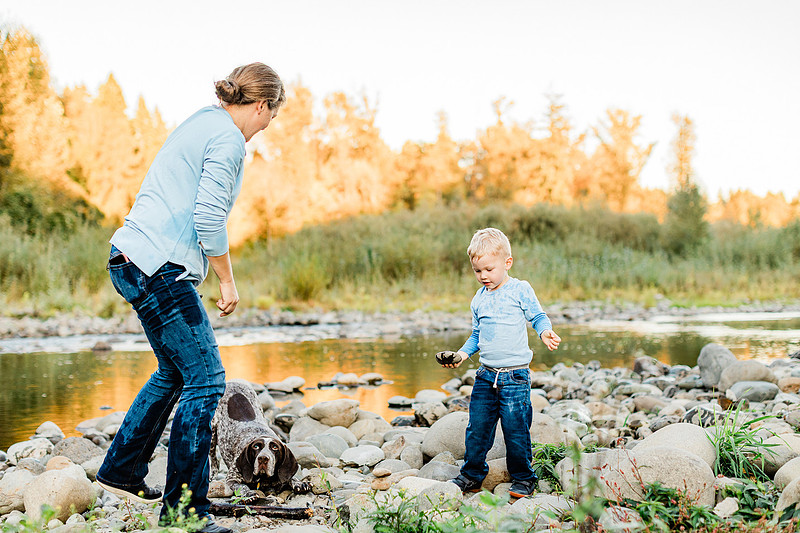 a boy, his mom and their dog playing by the river