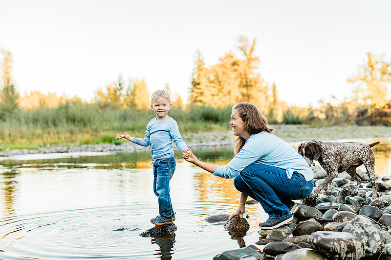 a boy, his mom and their dog playing by the river
