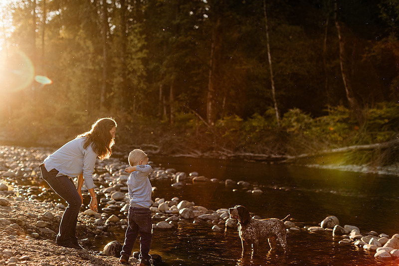 a boy, his mom and their dog playing by the river