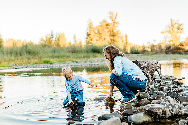 a boy, his mom and their dog playing by the river