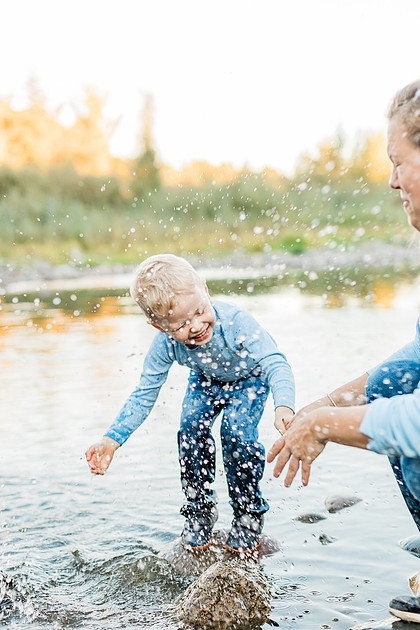 a boy, his mom and their dog playing by the river