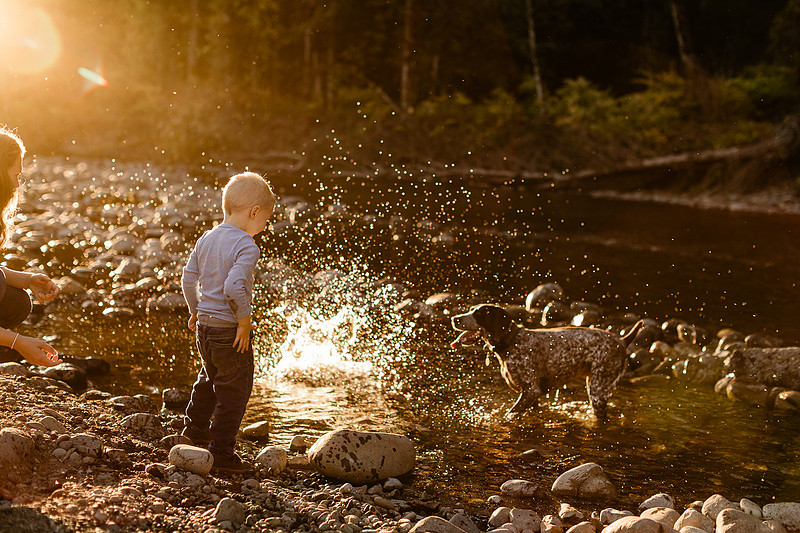a boy, his mom and their dog playing by the river
