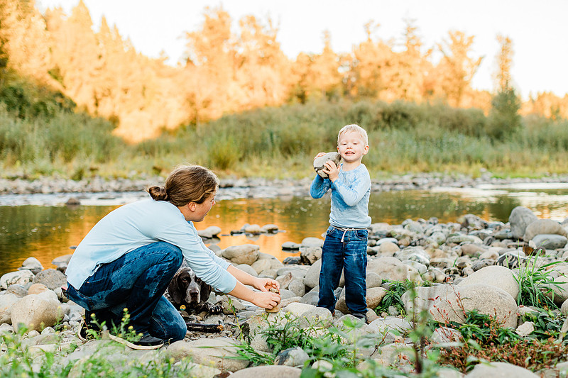 a boy, his mom and their dog playing by the river