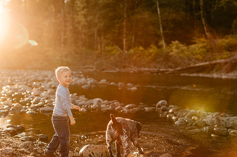 a boy, his mom and their dog playing by the river